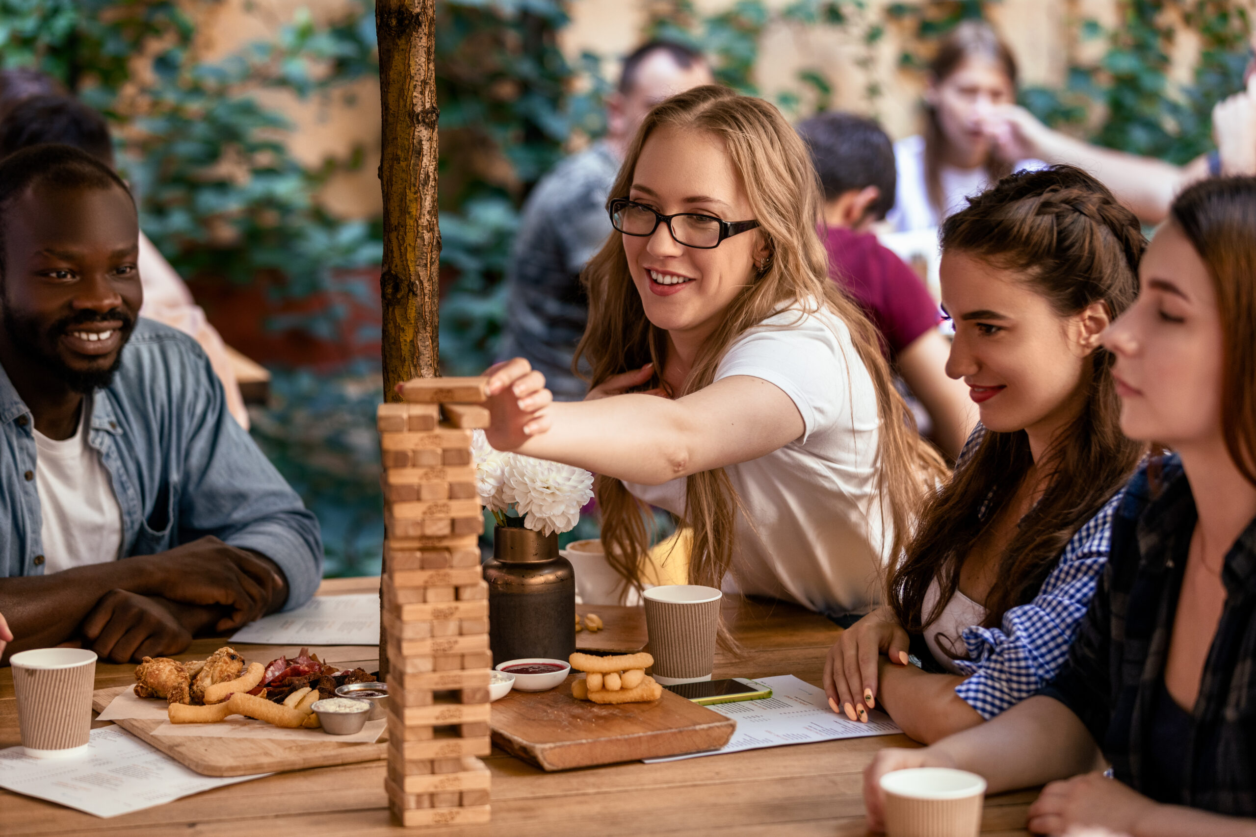 Caucasian girl is putting a brick to a tall tower at table game